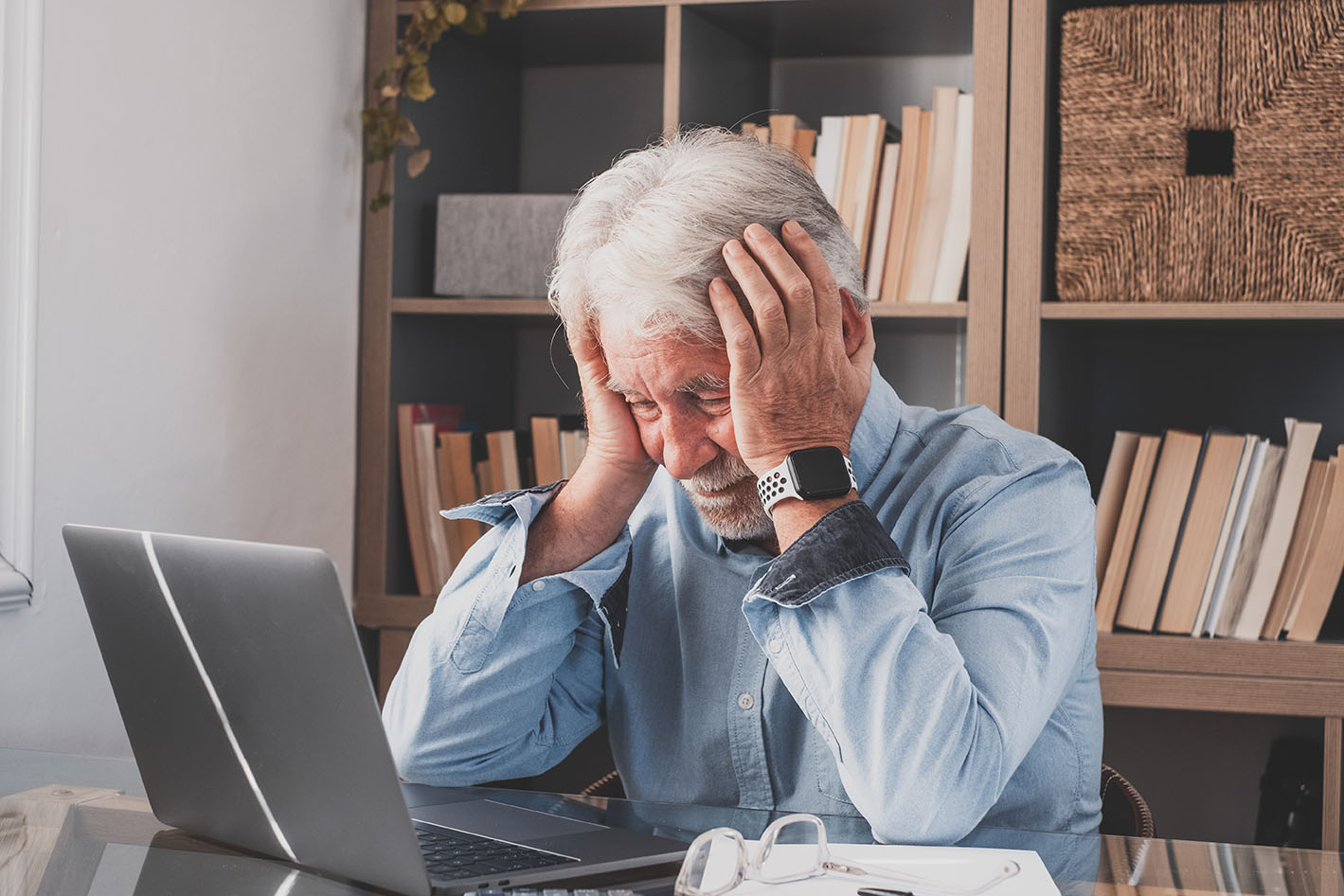 old businessman looking at laptop computer and holding his head in exasperation